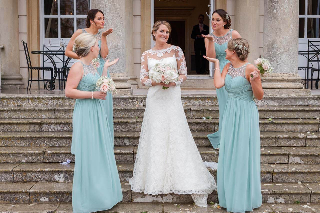bride smiling at camera with bridesmaids all blowing a kiss at bride