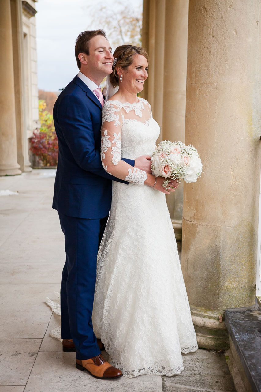 groom with arms around bride's waist standing looking out onto gardens