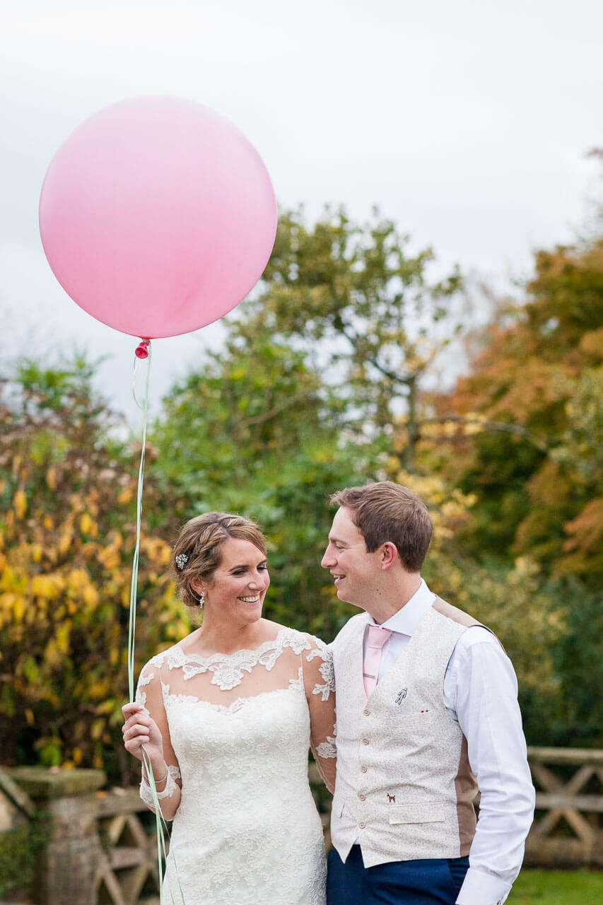 bride and groom walking looking at each other with bride holding large pink balloon