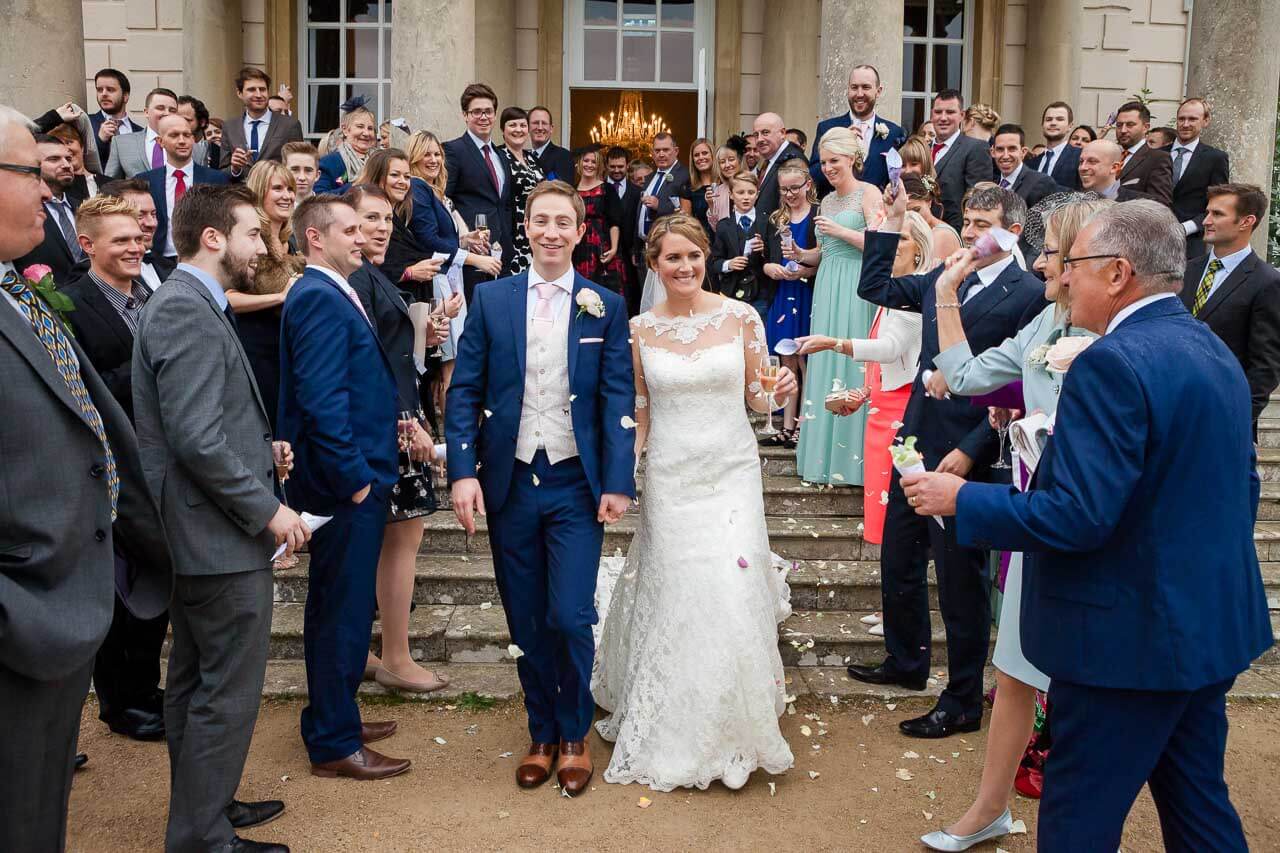 bride and groom walking towards camera with confetti being thrown at them