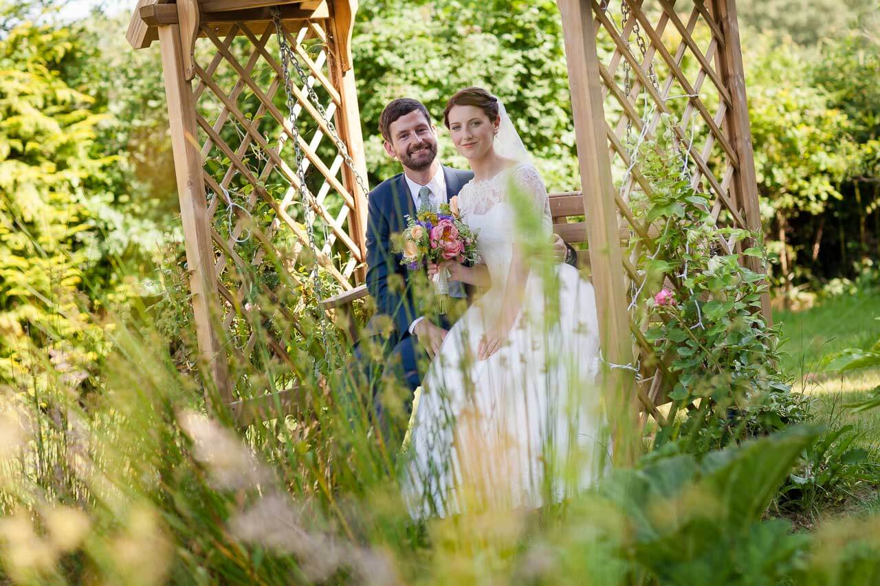 bride and groom sitting on seat in garden surrounded by flowers and plants