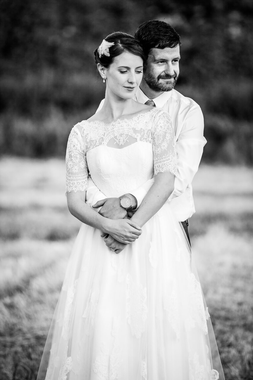 groom wraps his arms around bride who looks down for portrait shot