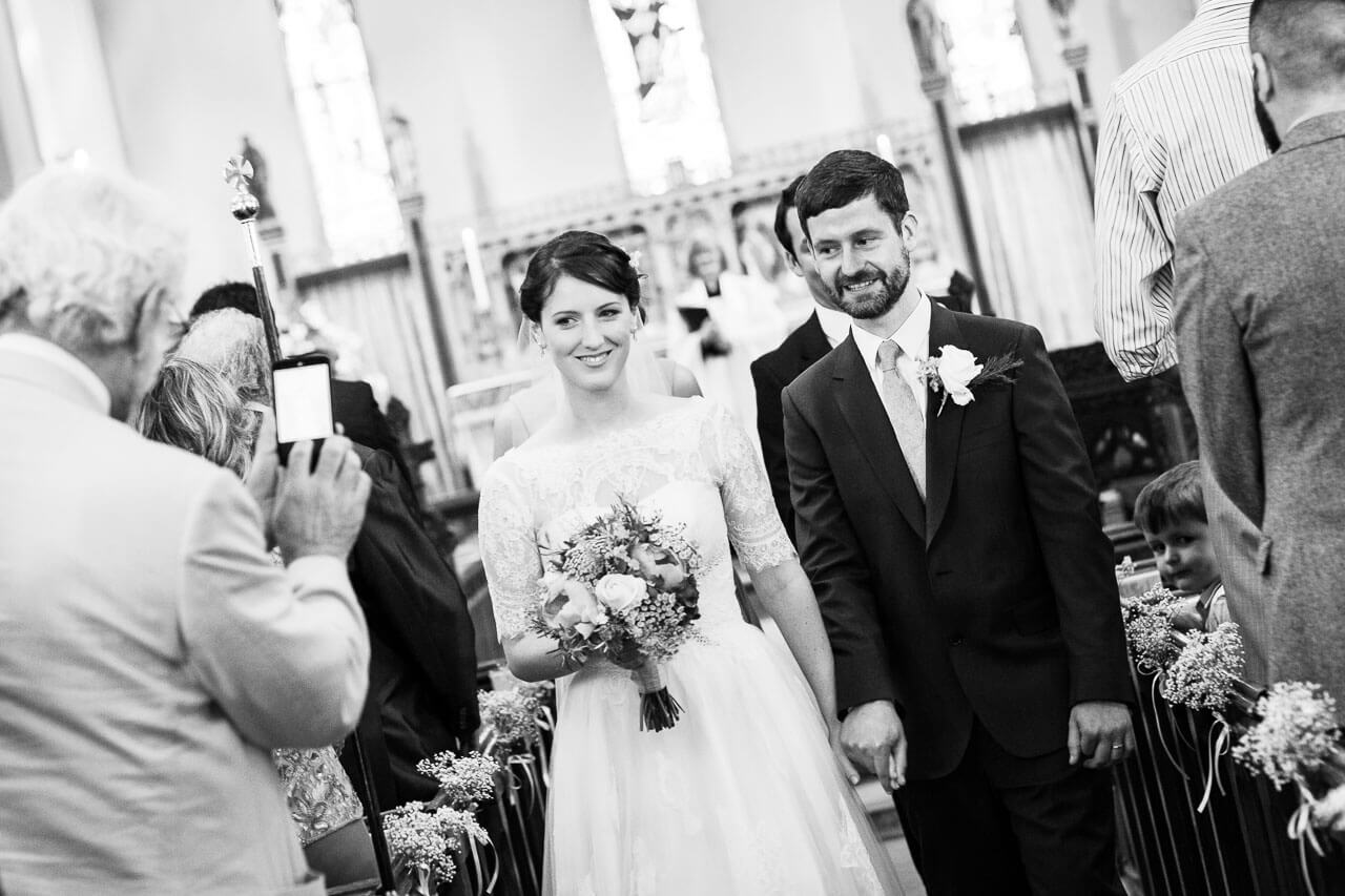 bride and groom walking back down the aisle smiling at guests