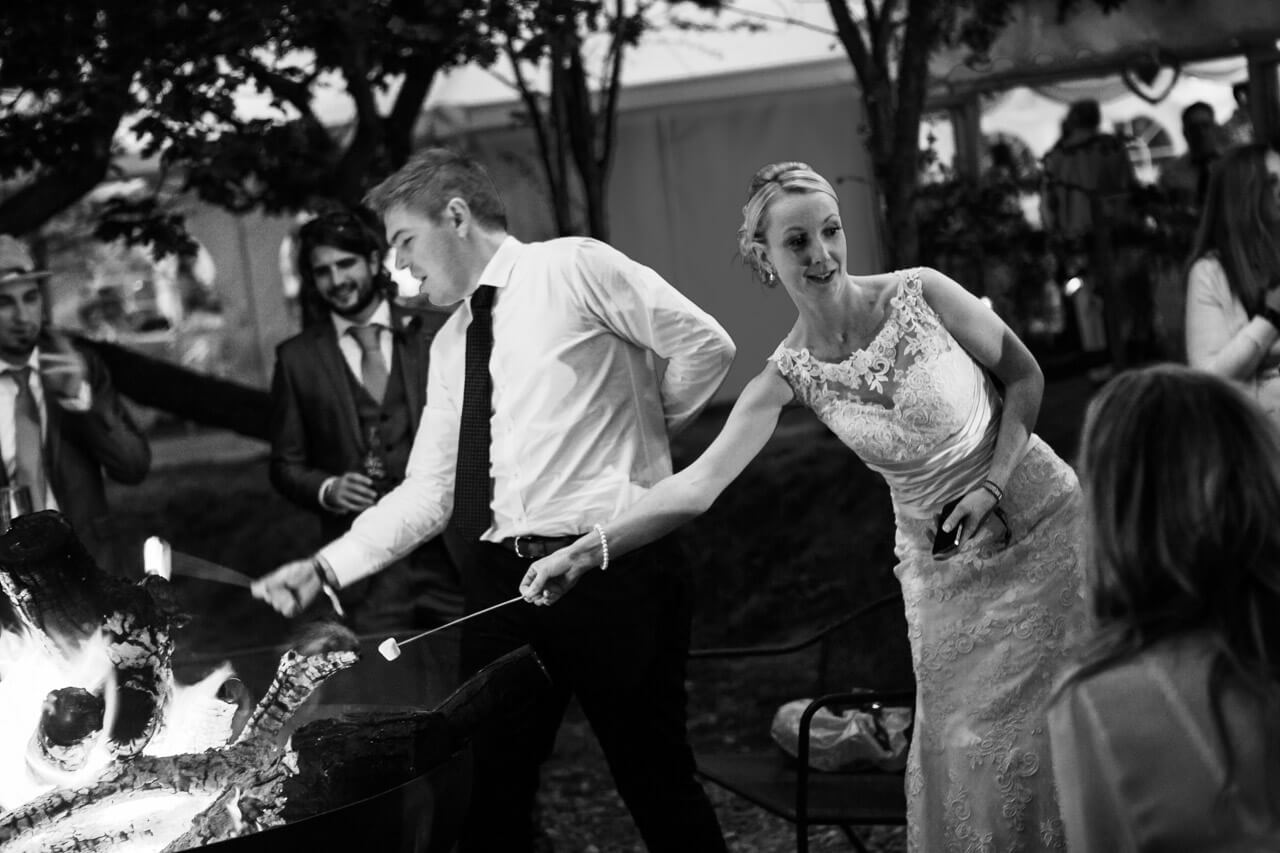 bride holds marshmallow stick into fire pit