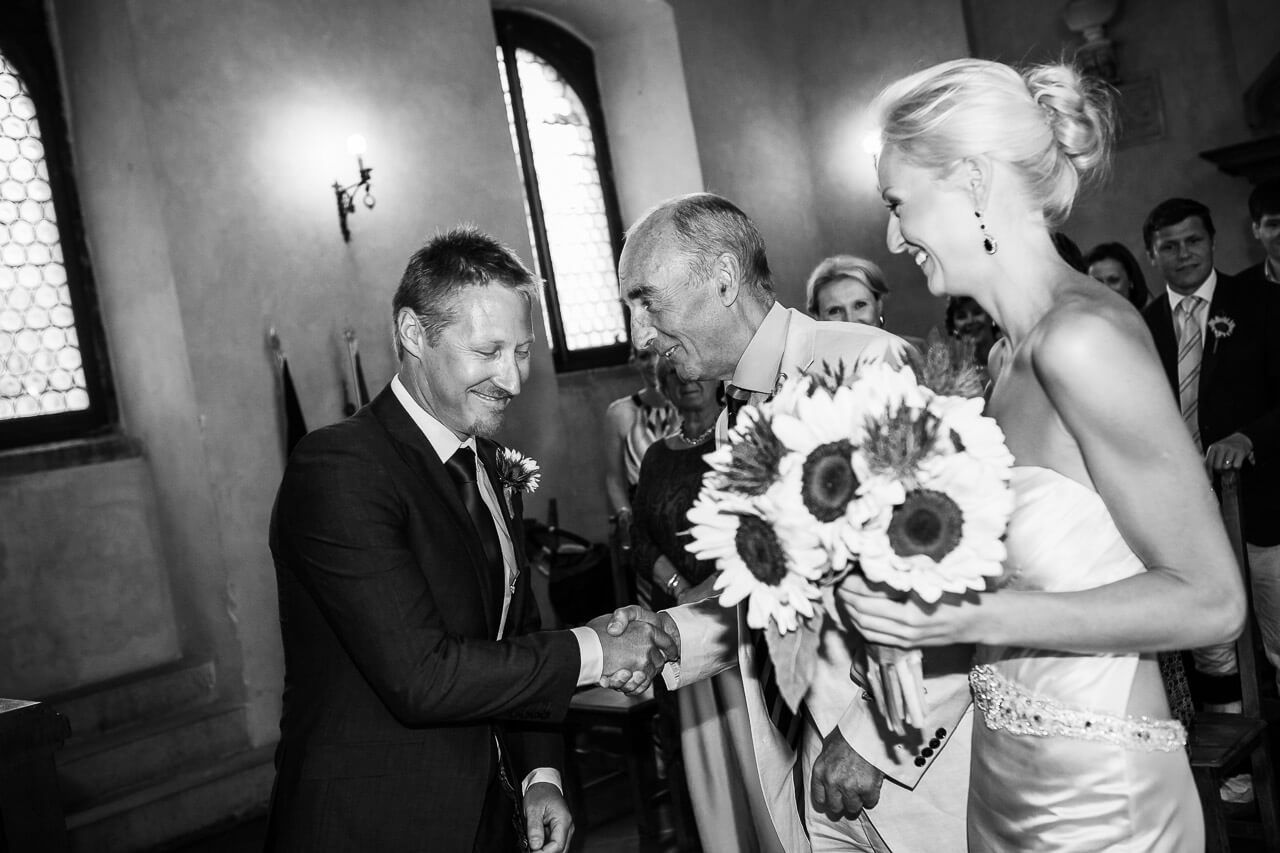 father of bride shakes hands with groom with bride looking on smiling