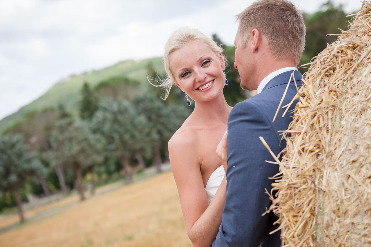 couple leaning against hay bale with bride smiling at camera