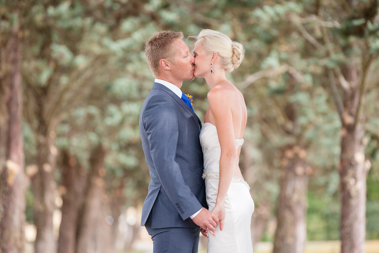 bride and groom kissing holding hands with trees blurred out in background
