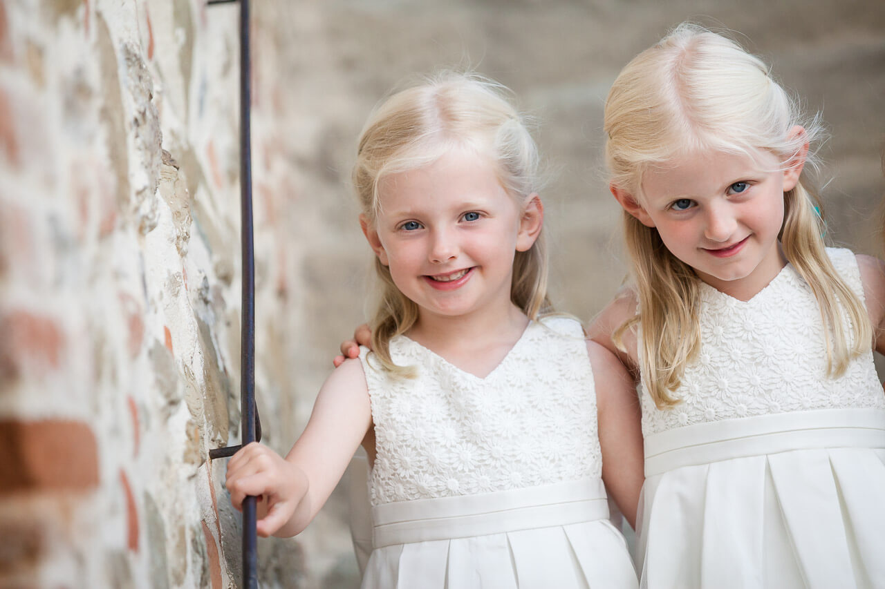 two flower girls in white dresses smiling looking at camera