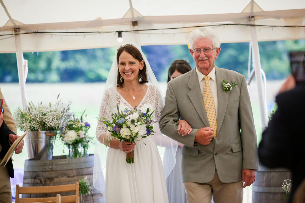 bride and father of the bride walking down aisle in marquee