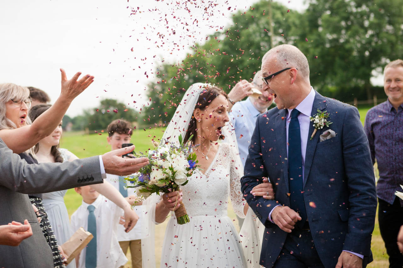 bride and groom walking into confetti with bride trying not to swallow confetti