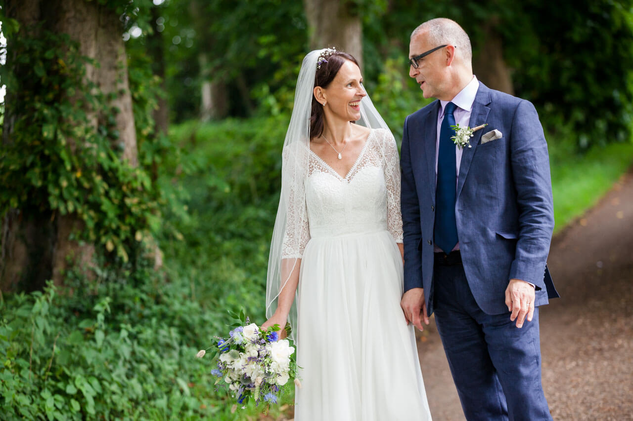 bride and groom walking along country lane talking and smiling at each other