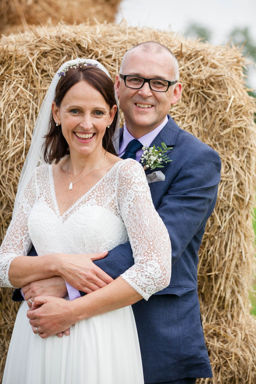 bride and groom in front of hay bales smiling at camera