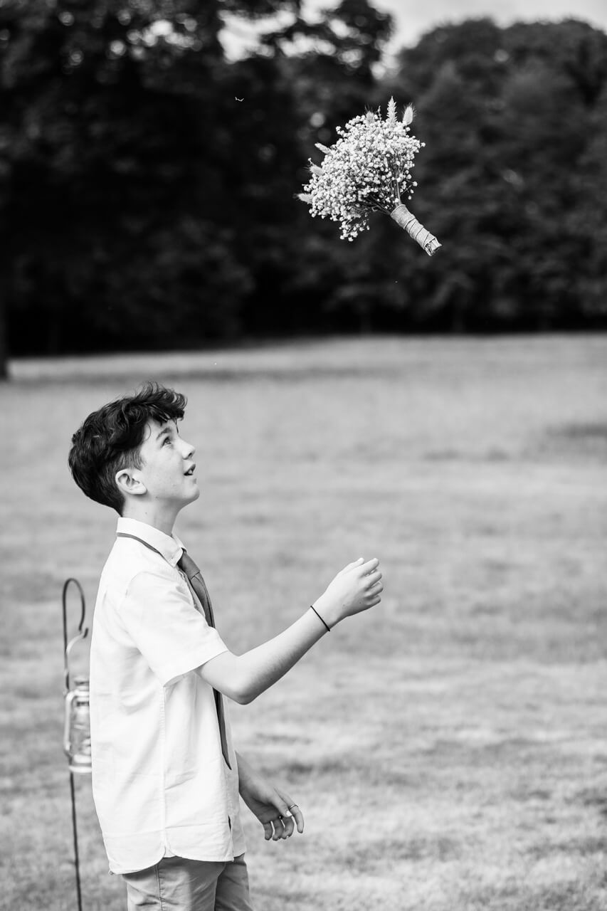page boy throwing bouquet of flowers up in the air