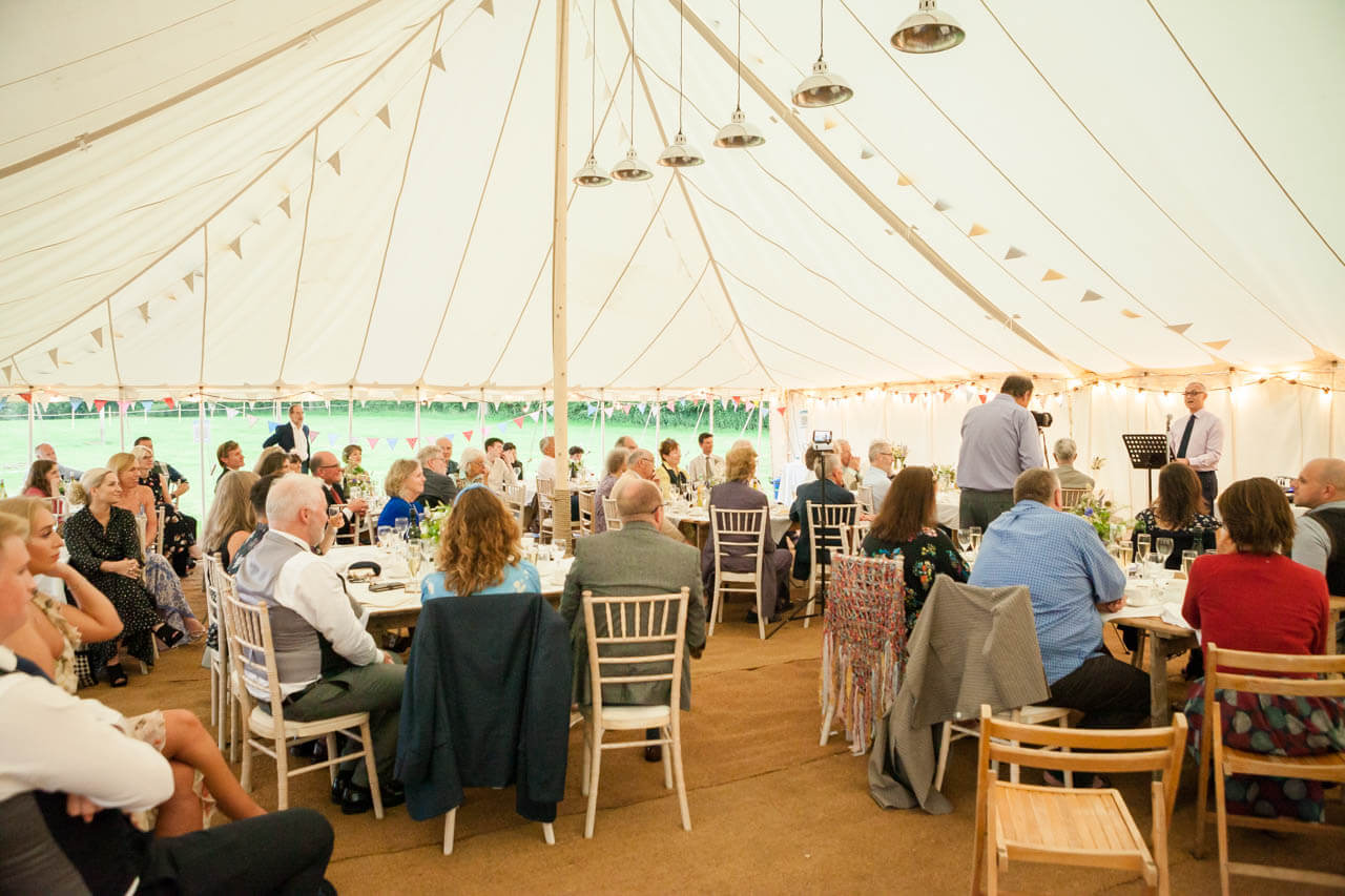 wide shot of marquee with guests listening to groom speech