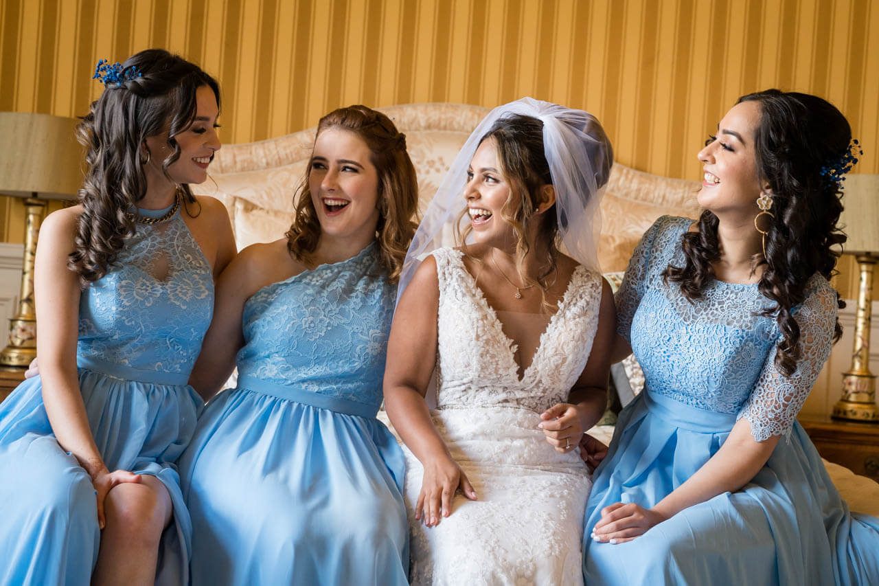bridesmaids and bride sitting on bed all smiling and looking at each other
