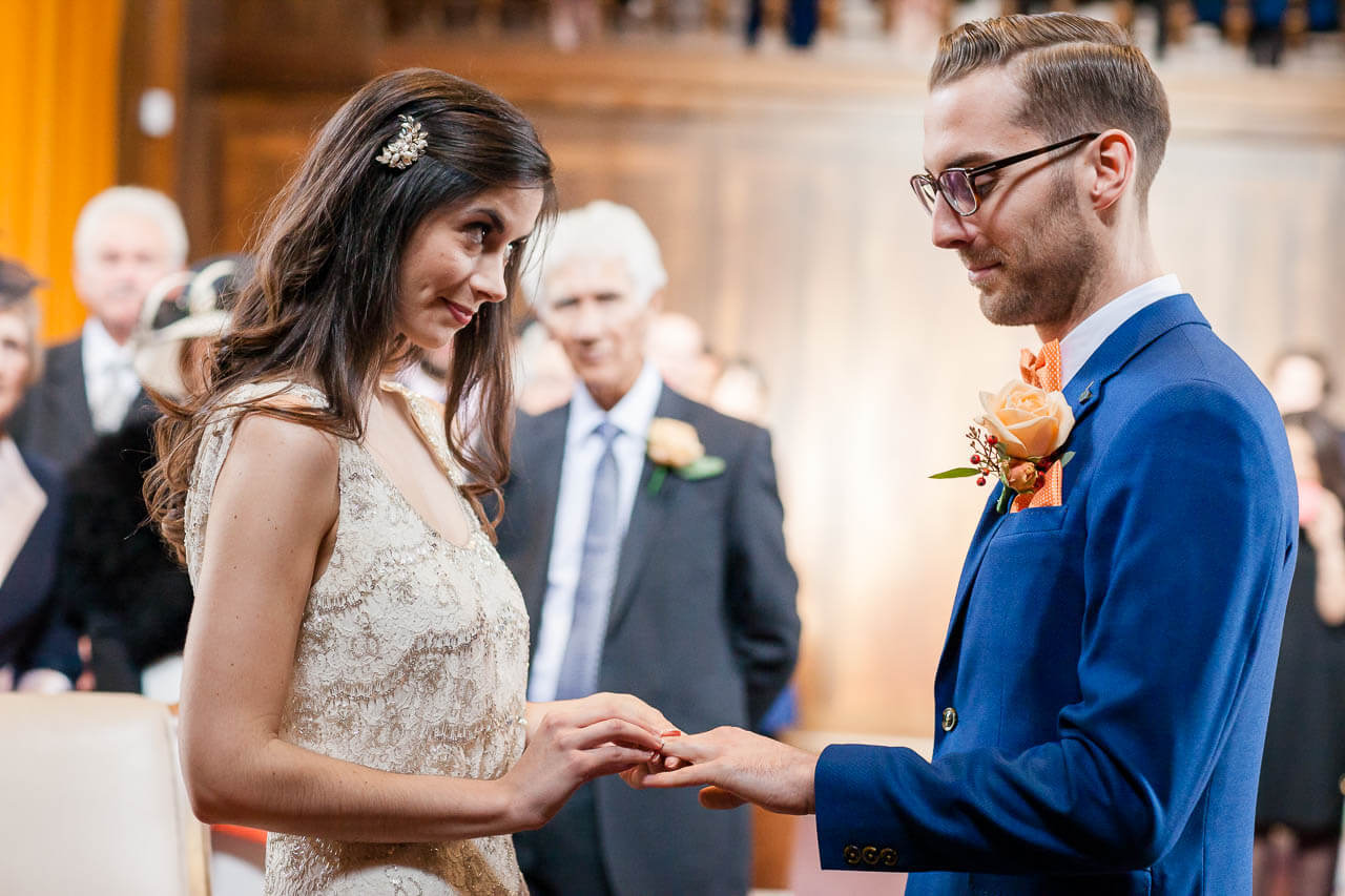 bride looks at groom while putting ring on