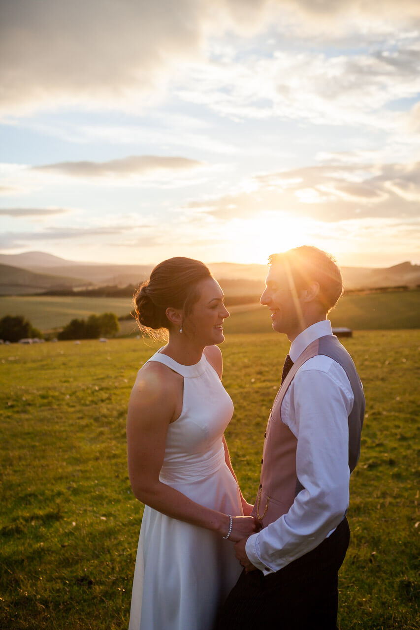 bride and groom smiling together sunset behind heads
