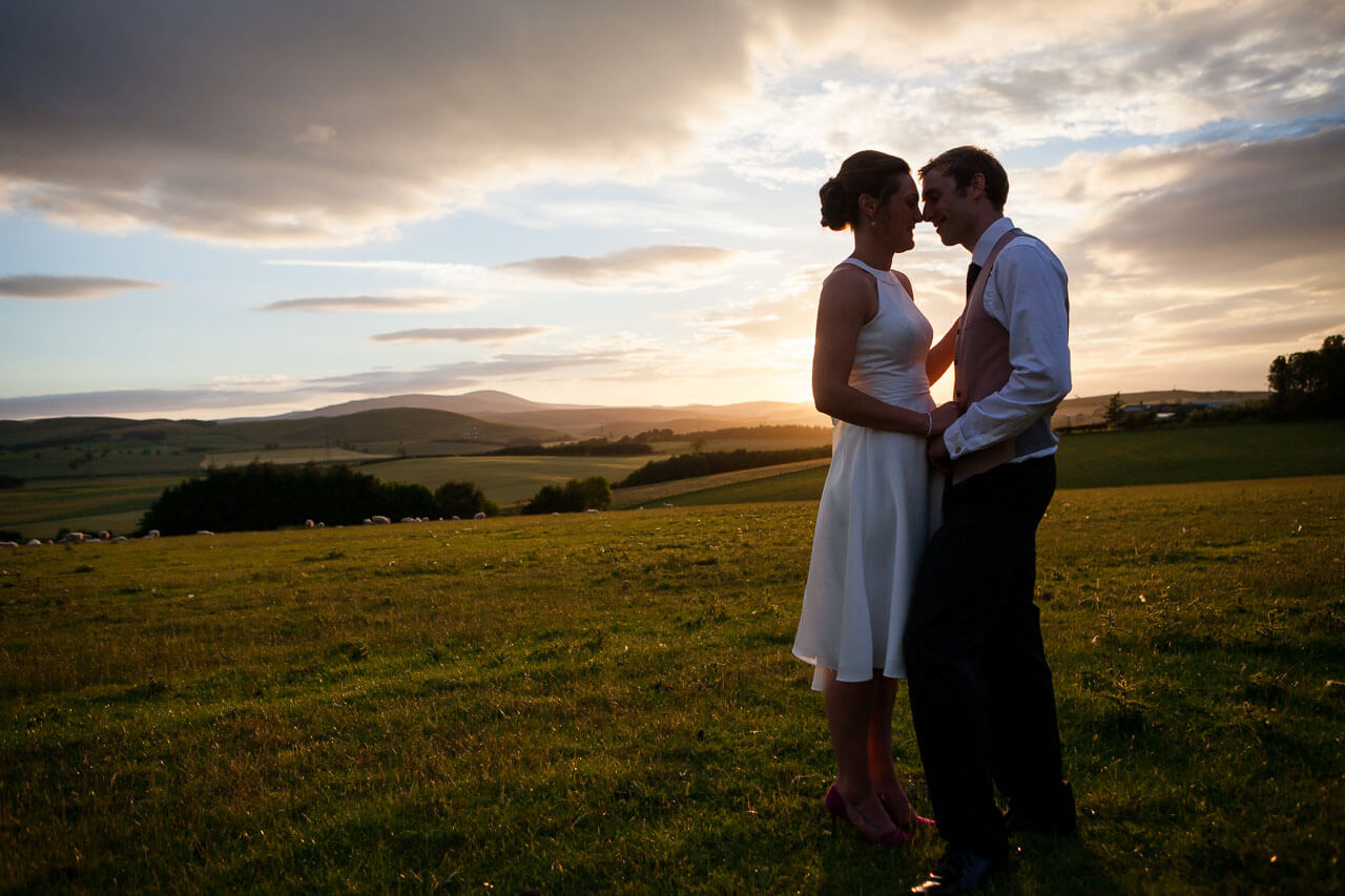 bride and groom facing each other sunset behind