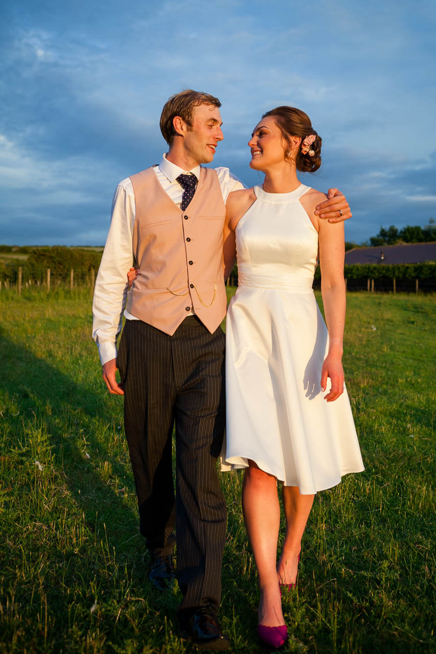 bride and groom walking towards the camera arm and arm sunset light on faces