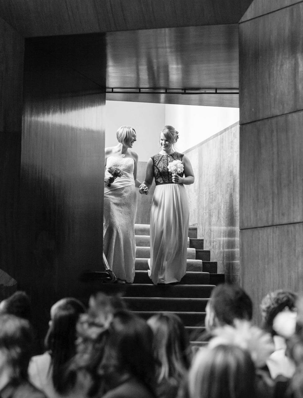 two brides walking down stairs towards guests in ceremony room