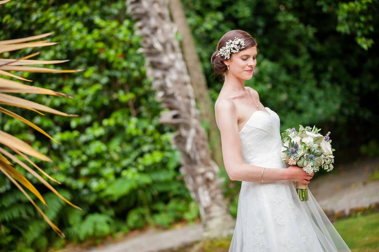 bride looking down holding bouquet with tropical greenery plants in backdrop