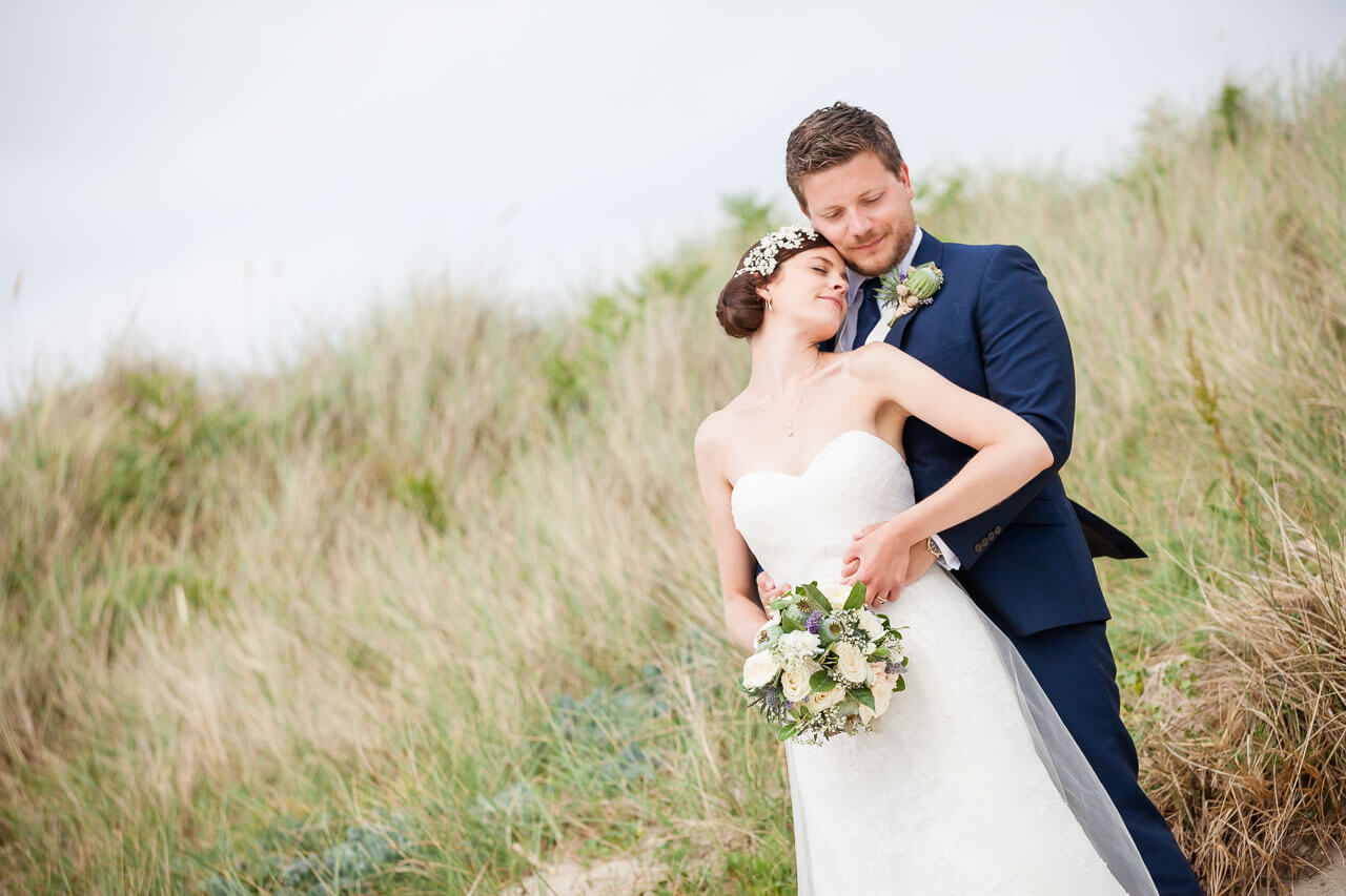 bride leaning back against groom with sand dunes in backdrop