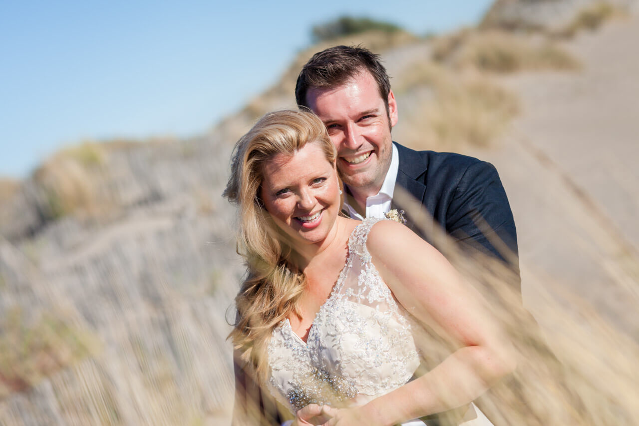bride and groom smiling looking at camera on beach