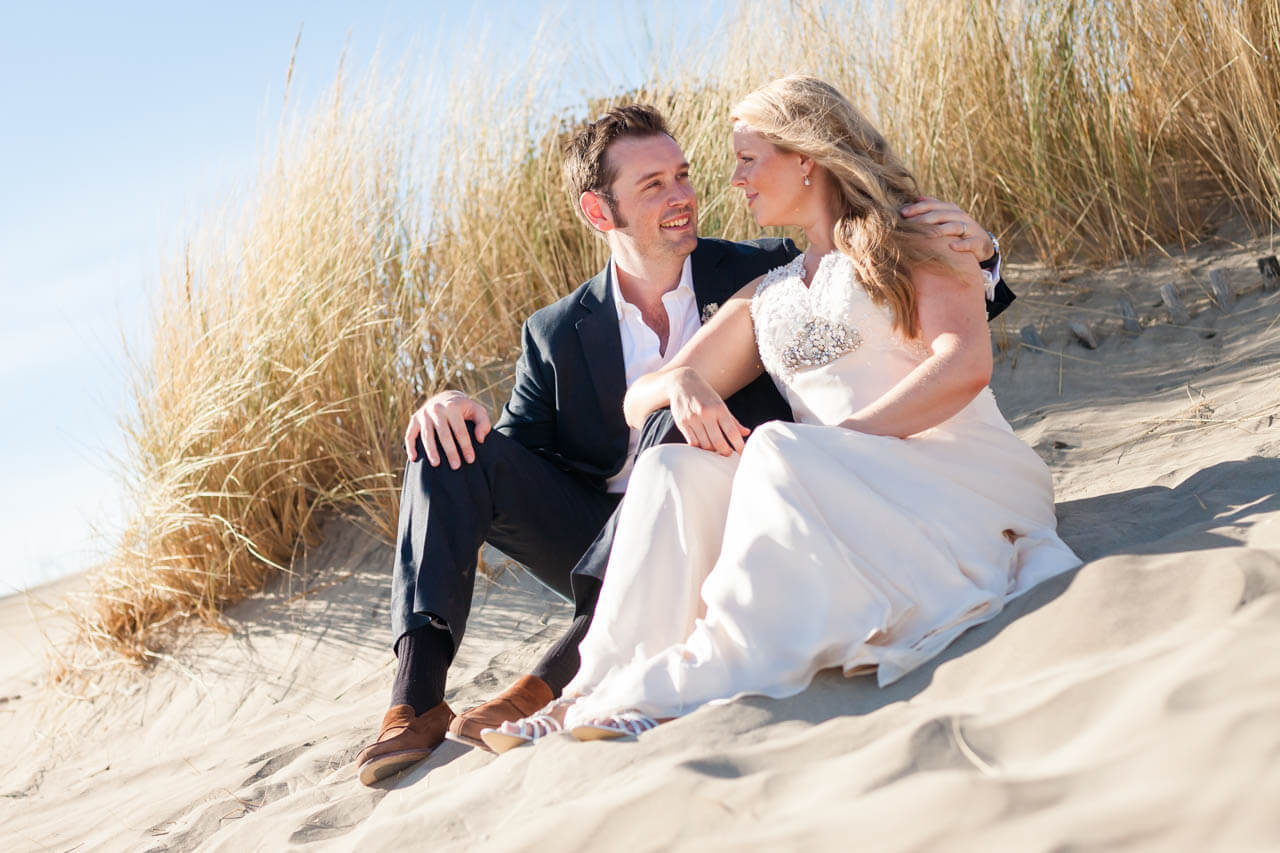 bride and groom sitting on beach looking at each other