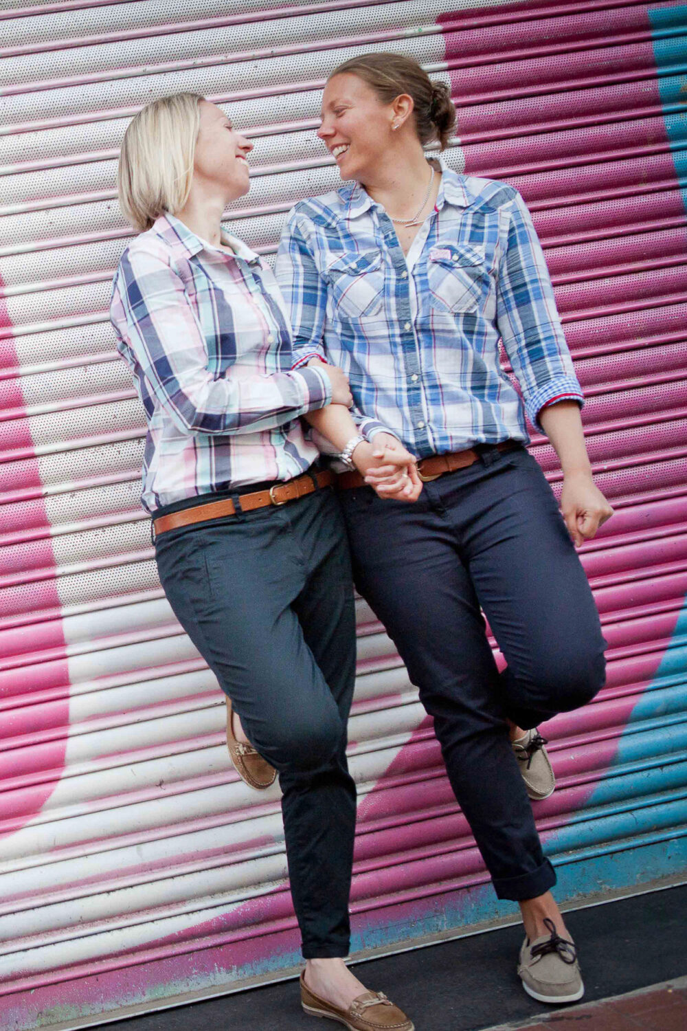 female couple stand against colourful backdrop laughing together