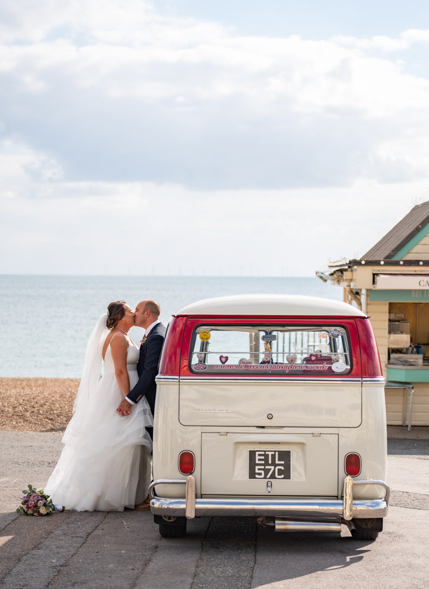 couple kissing leaning against campervan with sea in background