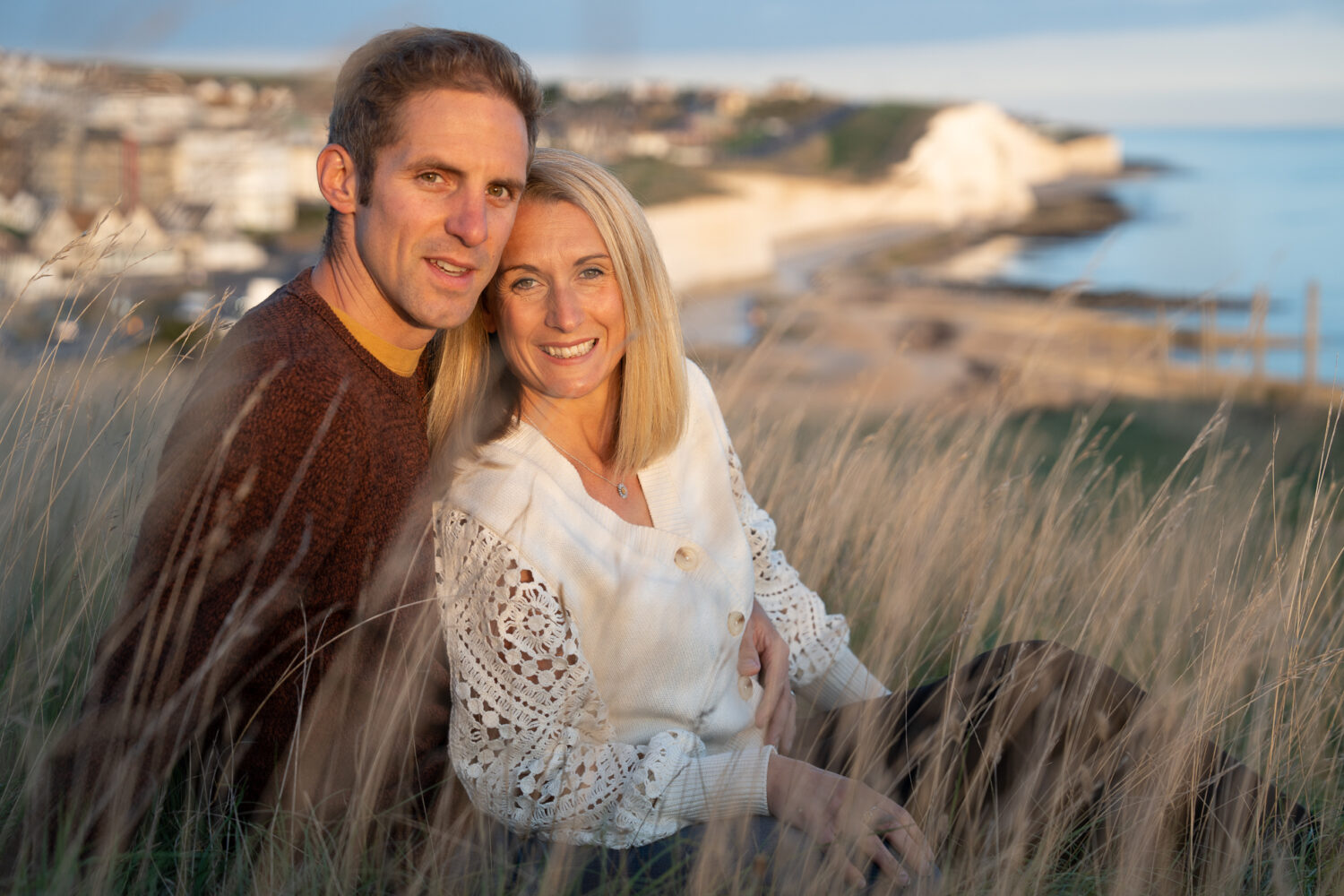 couple looking into camera sitting in long grass during golden hour