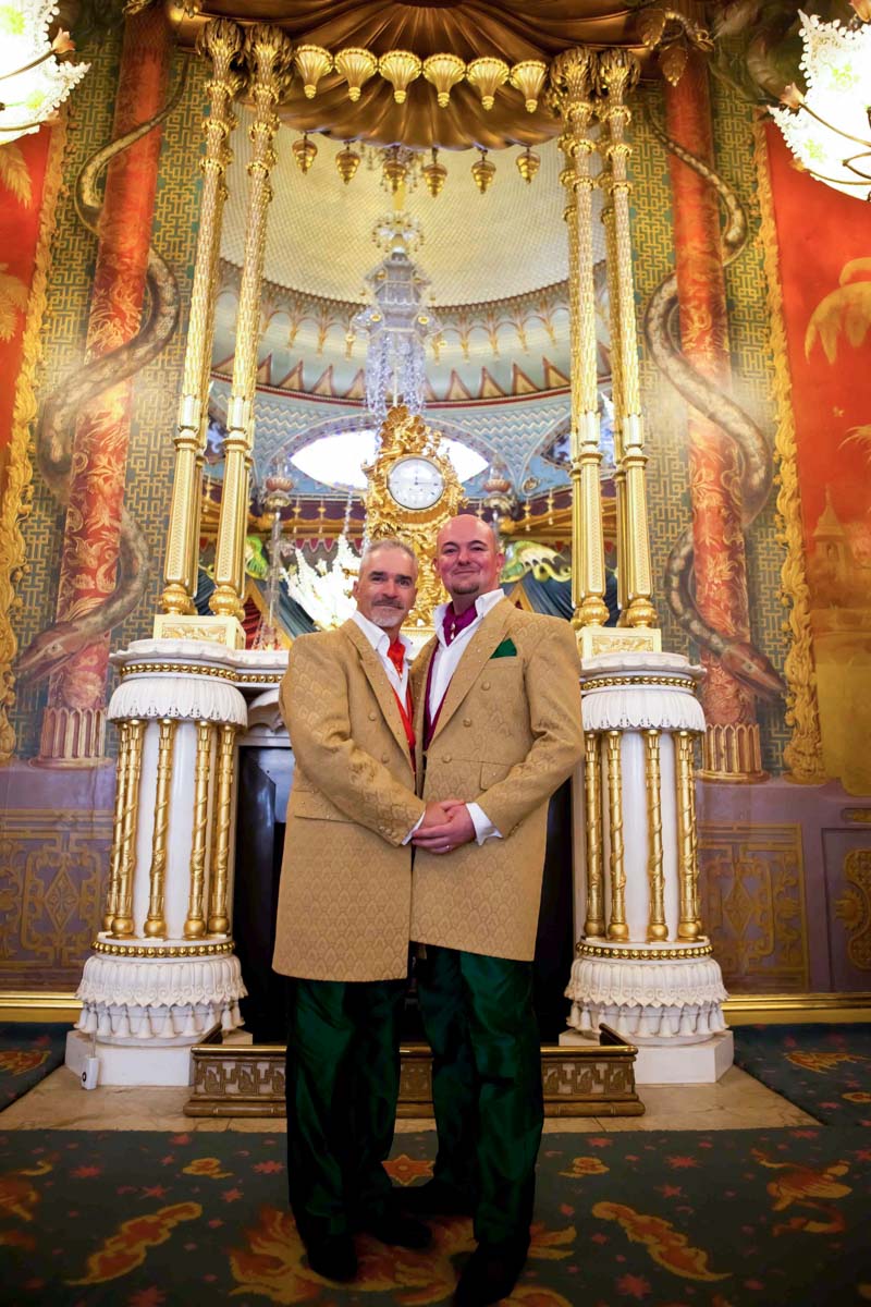 inside the Royal Pavilion orange and red interiors with grooms standing holding hands looking towards camera