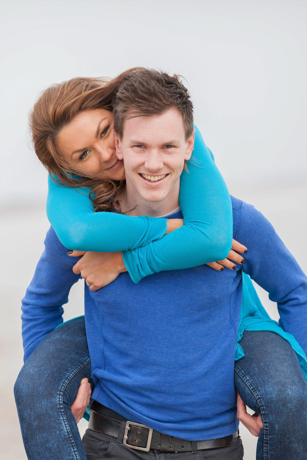 man gives fiancee piggy back both smiling looking into camera