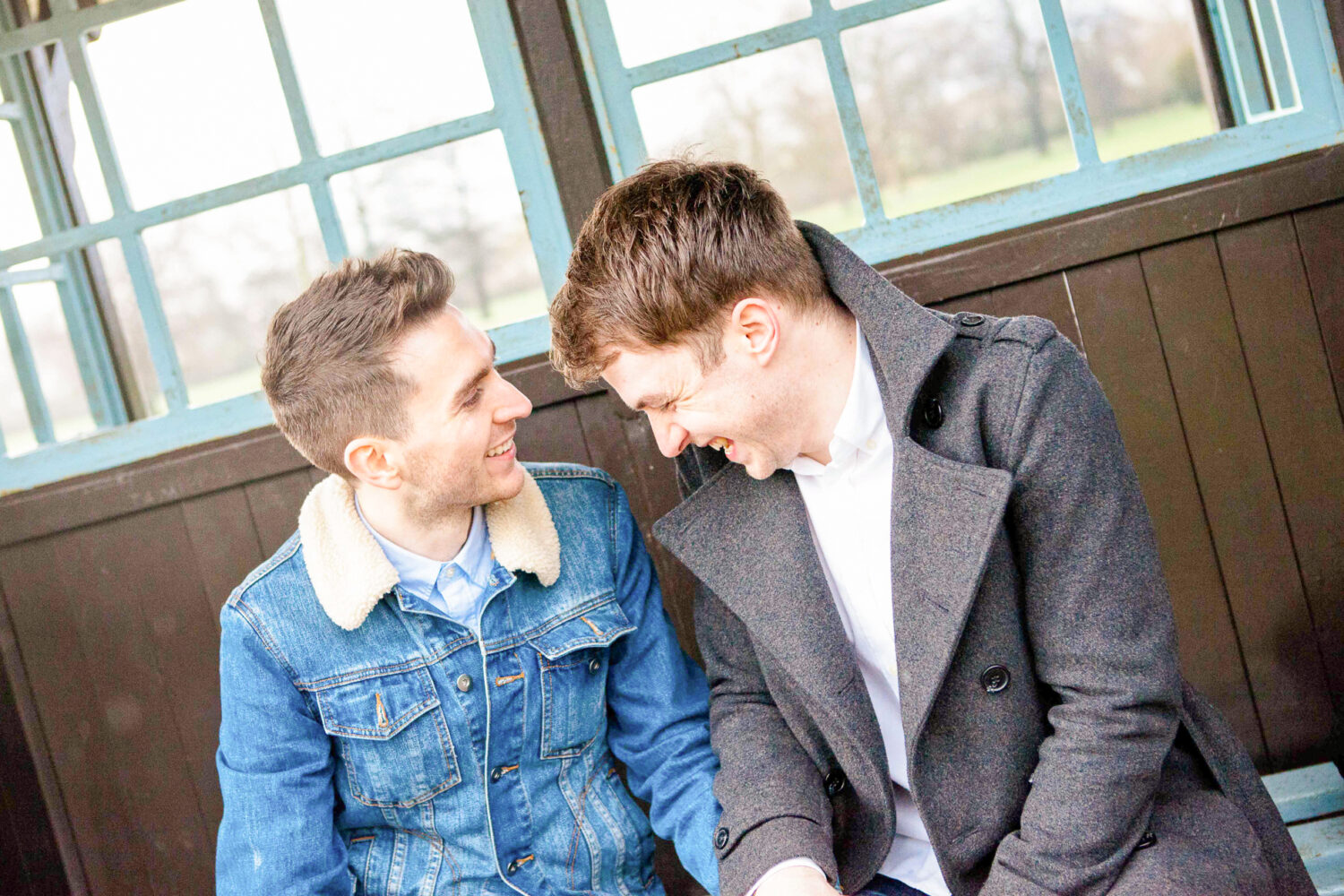 two guys sitting laughing in bus stop looking at each other