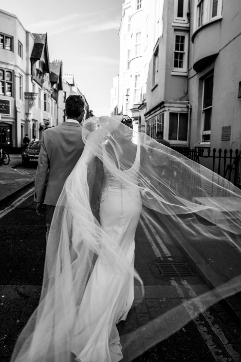 bride and groom walking away from the camera on a windy wedding day with veil flying in the wind