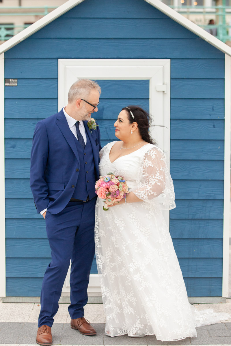bride and groom standing outside beach hut looking at each other smiling