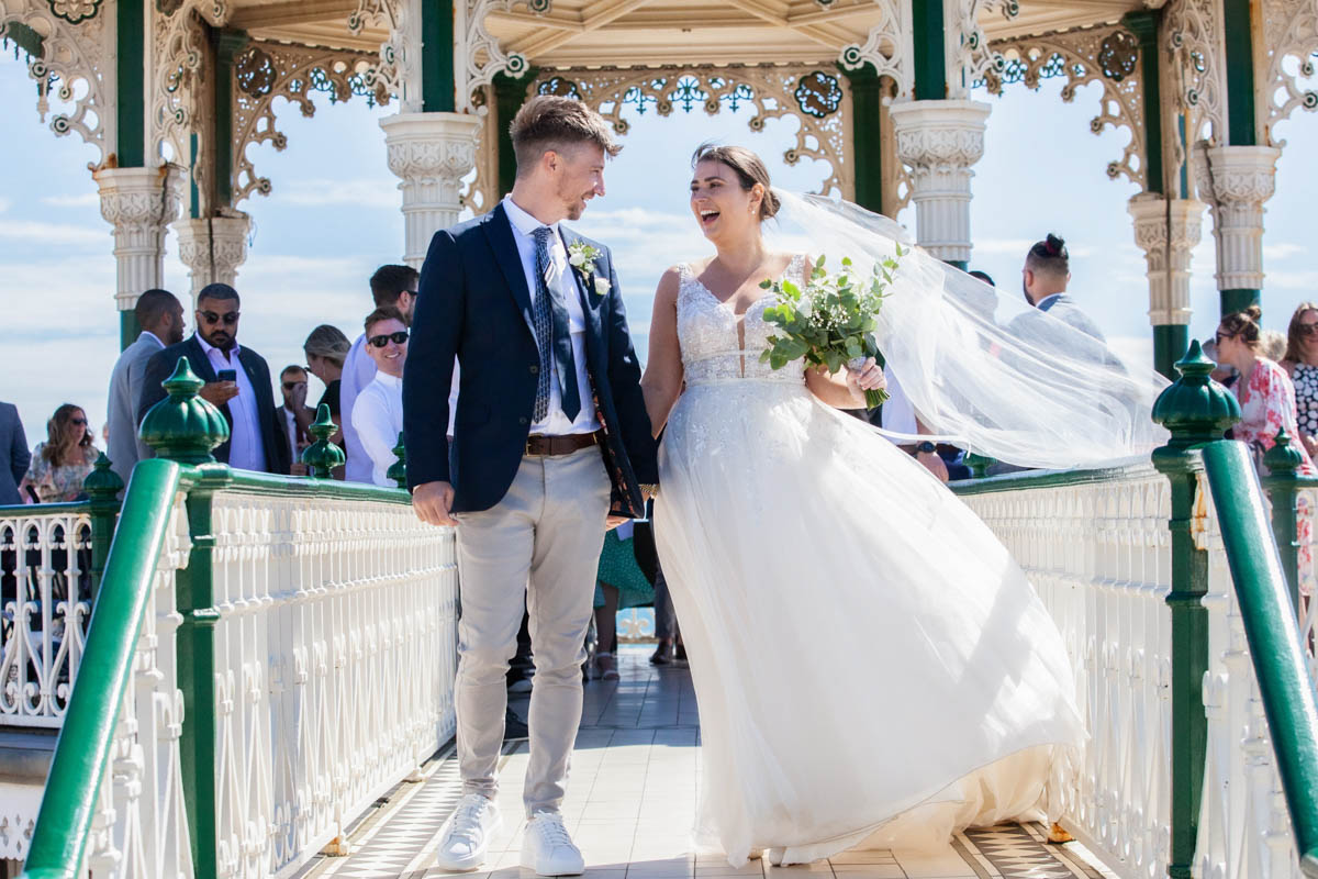 bride and groom walking towards end of Brighton bandstand looking at each other smiling