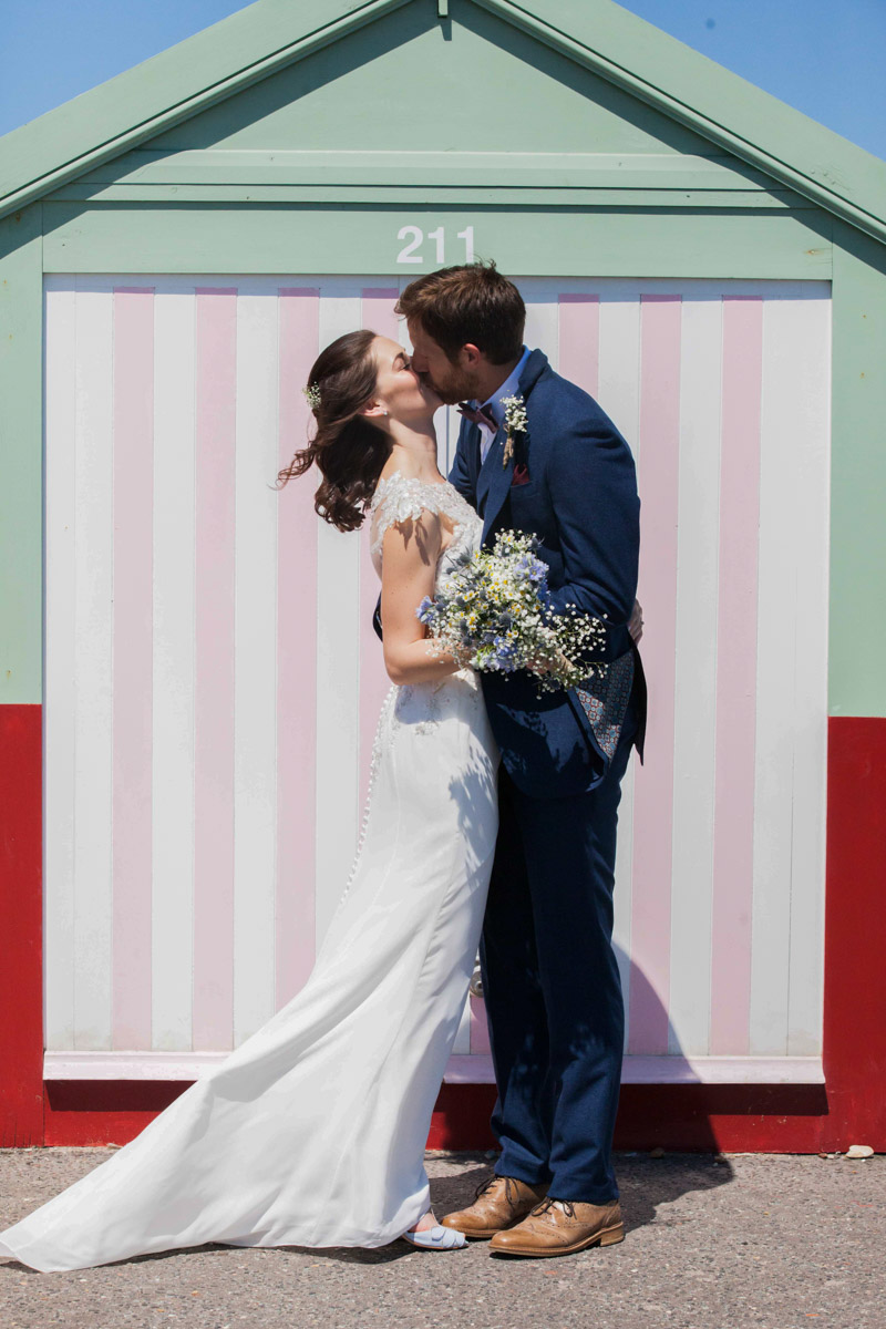 couple kissing standing in front of Brighton beach hut