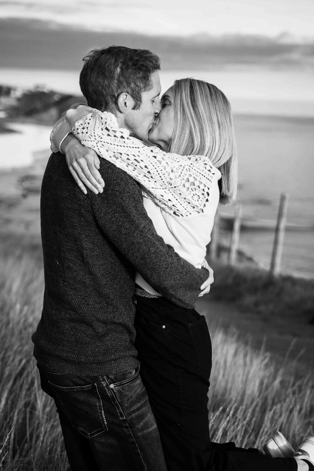 man lifts woman as she wraps her arms around his neck as they kiss