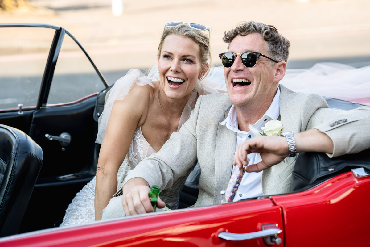 bride and groom cruising around in a red mustang laughing at a joke