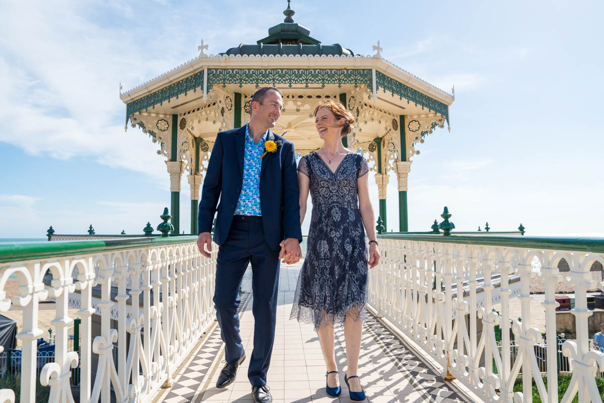 bride and groom walk towards camera with bandstand in background