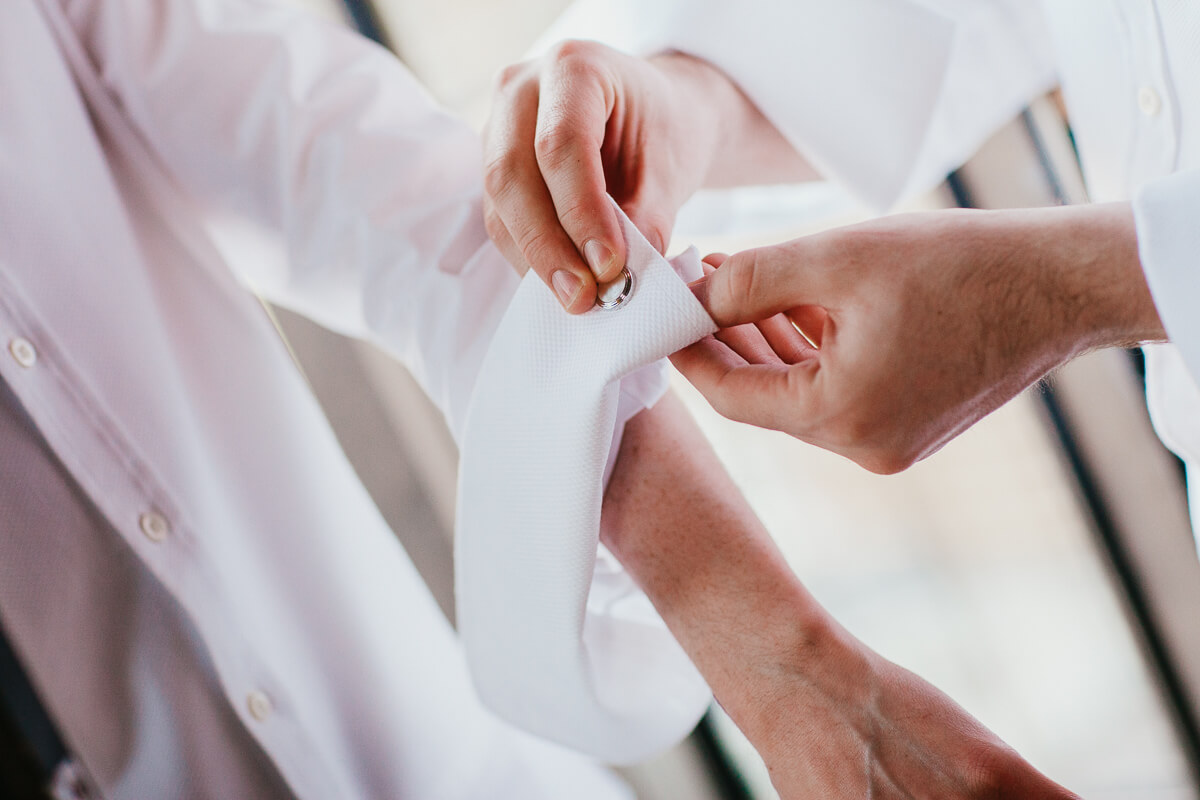 close up of two grooms doing up cufflinks