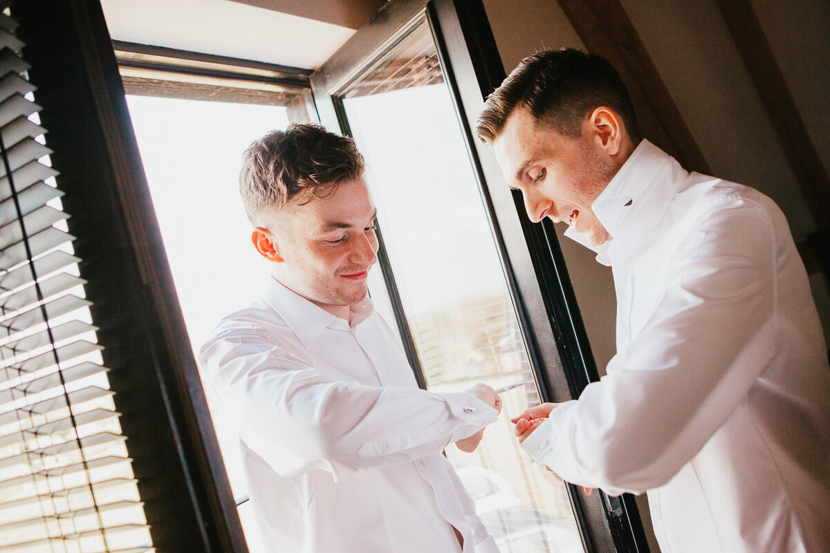 two grooms doing each others cufflinks on