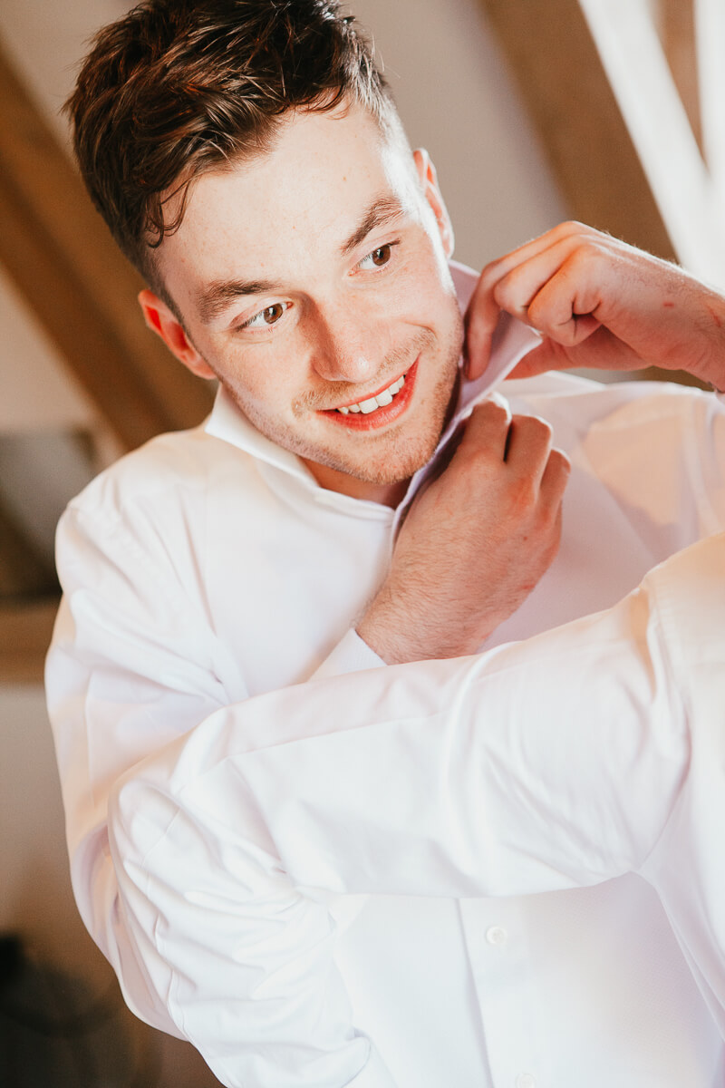 groom doing up his top button on shirt with a smile
