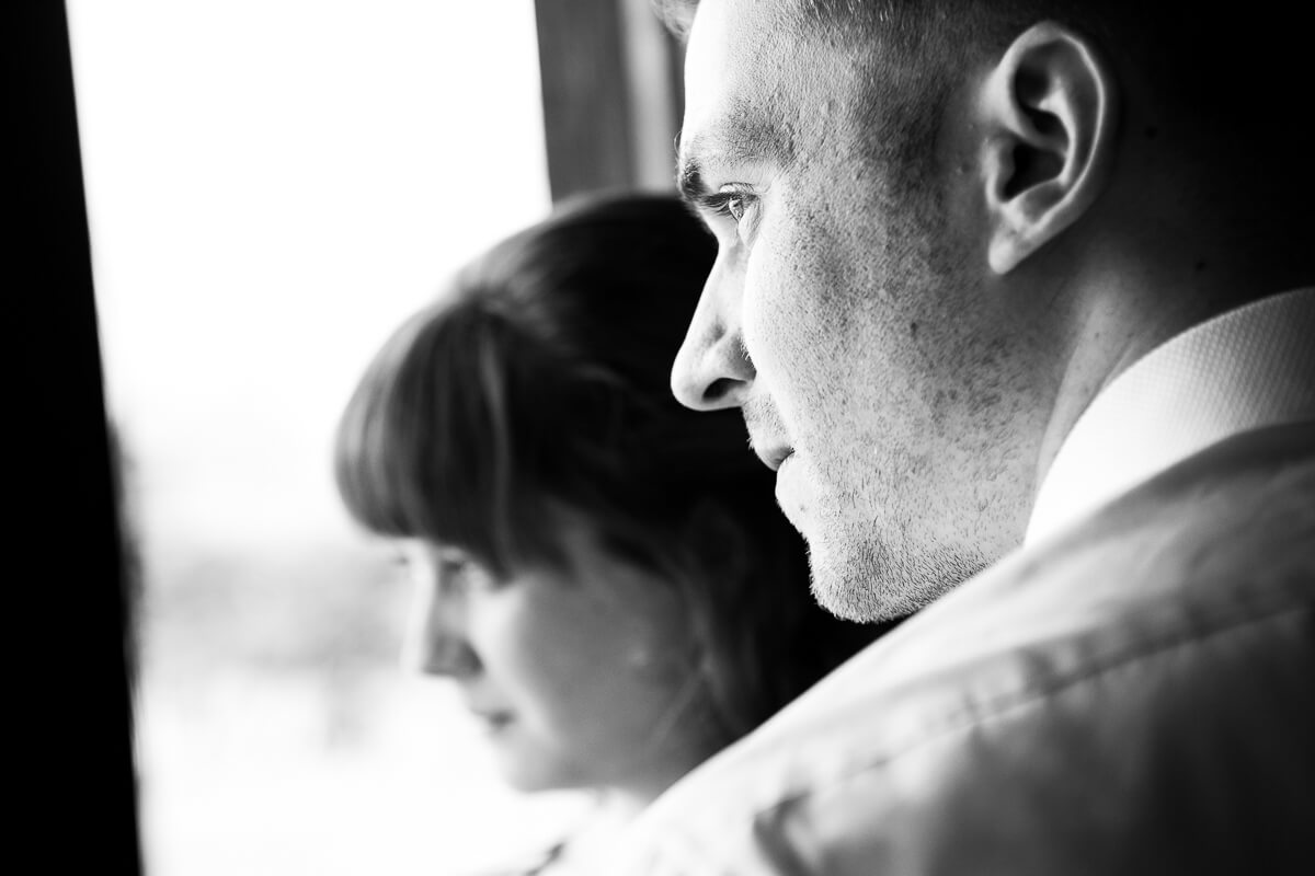 close up portrait of groom looking out of window with bridesmaid out of focus in the background