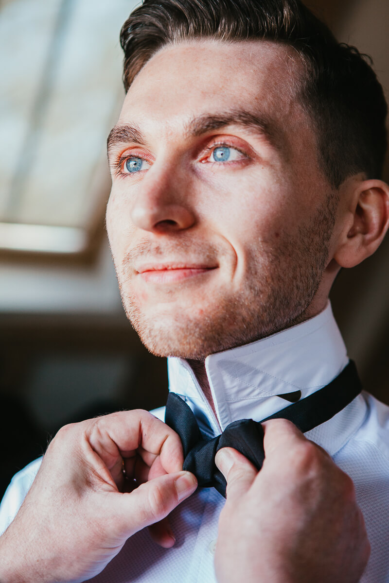 close up of a groom having his tie done up by his partner