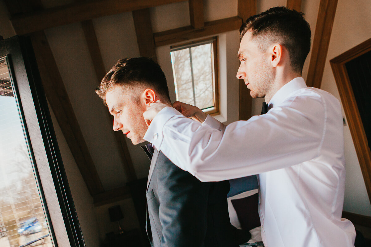 grooms standing behind each other doing final touches doing up shirt collar