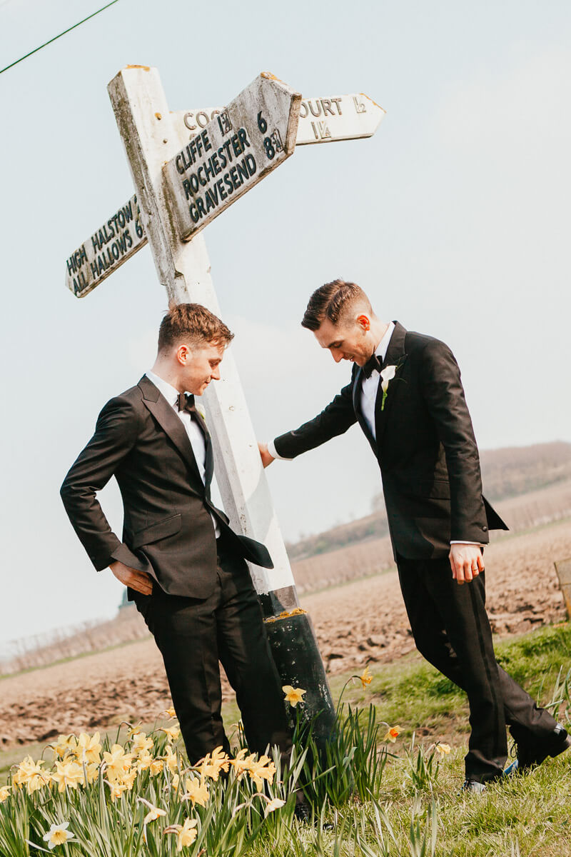 cool looking grooms in tuxedoes standing either side of wooden sign post