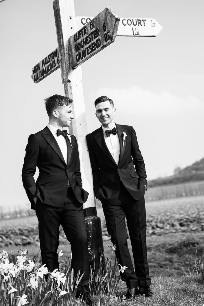 two grooms standing either side of a sign post with hands in pockets looking very cool