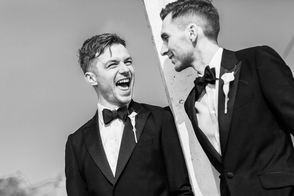 groom laughing loudly with the other groom looking at each other